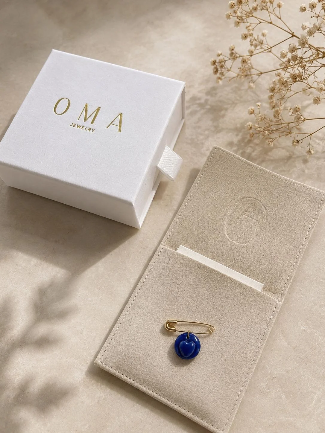 The blue pendant on its safety pin beside the OMA case and suede pouch